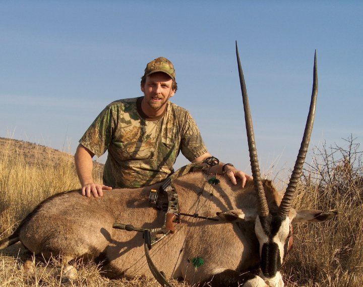 Hunter in camouflage kneeling beside a harvested gemsbok oryx during an African bowhunting trip