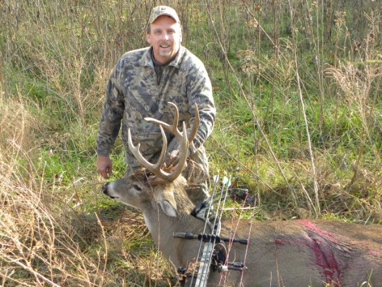 Smiling hunter in camouflage kneeling beside a harvested trophy whitetail buck with large antlers