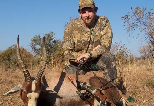 Hunter kneeling beside a blesbok trophy with compound bow in the African bush