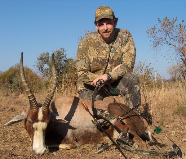 Hunter kneeling behind a blesbok trophy with compound bow, African bushveld background