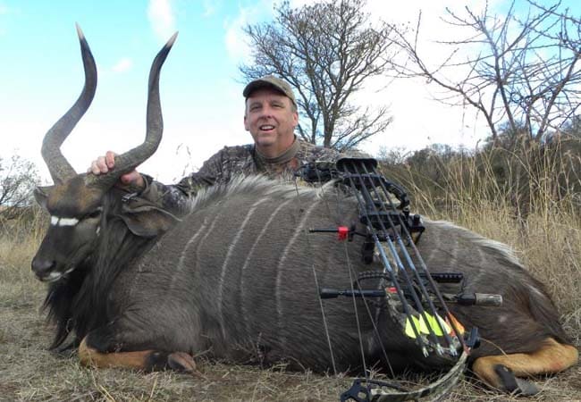 Bowhunter smiling with harvested nyala antelope and compound bow in South African bush