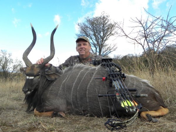 Hunter smiling with compound bow beside a harvested nyala antelope in South Africa