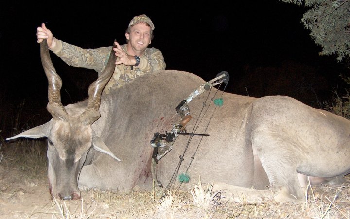 Hunter kneeling beside a large eland trophy with compound bow, nighttime photo