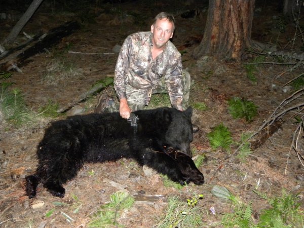 Hunter kneeling beside a harvested black bear in a nighttime forest setting