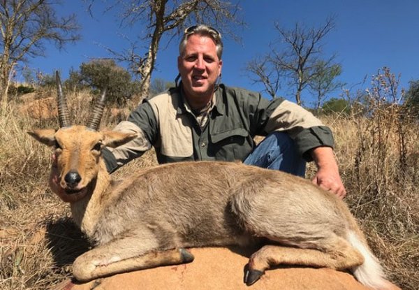 Hunter kneeling behind a harvested antelope with curved horns in a South African bushveld setting