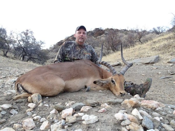 Hunter in camouflage kneeling behind a harvested impala on a rocky hillside