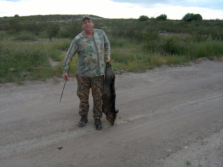 Hunter in camouflage holding a harvested javelina on a rural dirt road