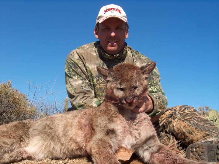 Hunter in camouflage kneeling beside a harvested mountain lion in the desert