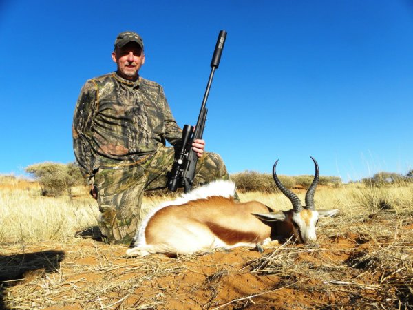 Hunter in camouflage kneeling beside a springbok trophy with a rifle in the African bush