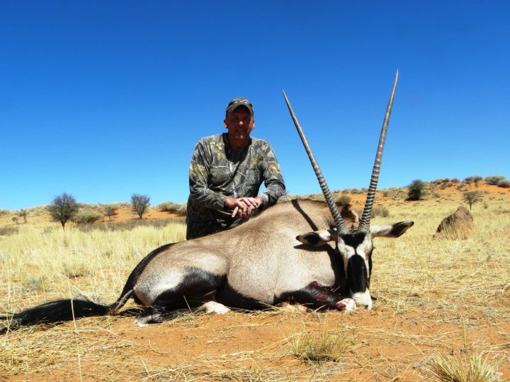 Hunter kneeling behind a harvested gemsbok oryx with long straight horns in Namibia desert