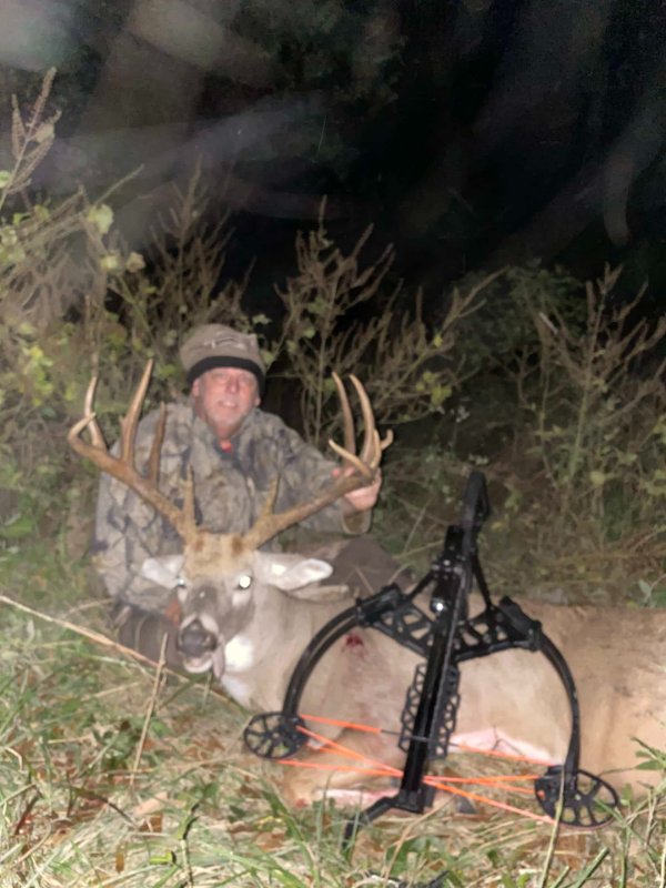 Hunter kneeling behind a harvested whitetail buck with a crossbow at night in the woods