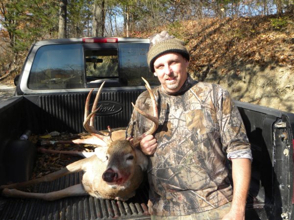 Smiling hunter in camo holding antlers of a whitetail buck in a pickup truck bed