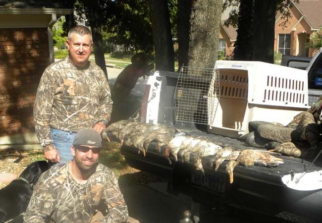 Two hunters in camo standing and kneeling beside a truck tailgate with a successful duck hunting harvest