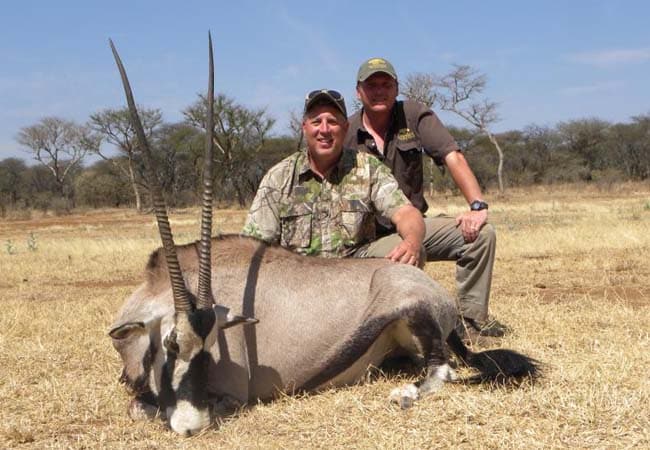 Two hunters kneeling behind a gemsbok oryx trophy on the African savanna