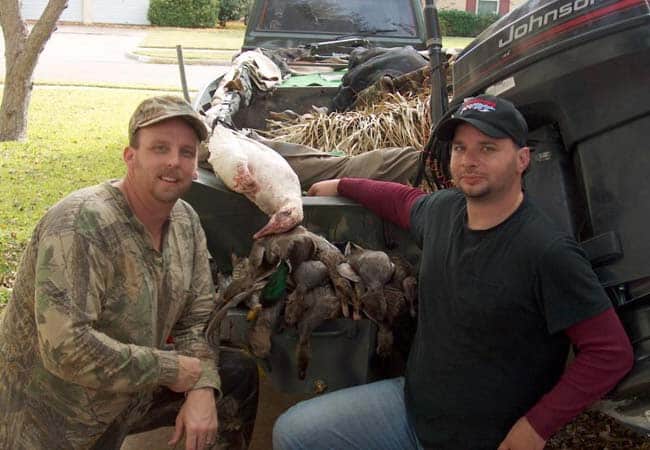 Two hunters kneeling by truck bed showing off a successful waterfowl hunt with harvested ducks